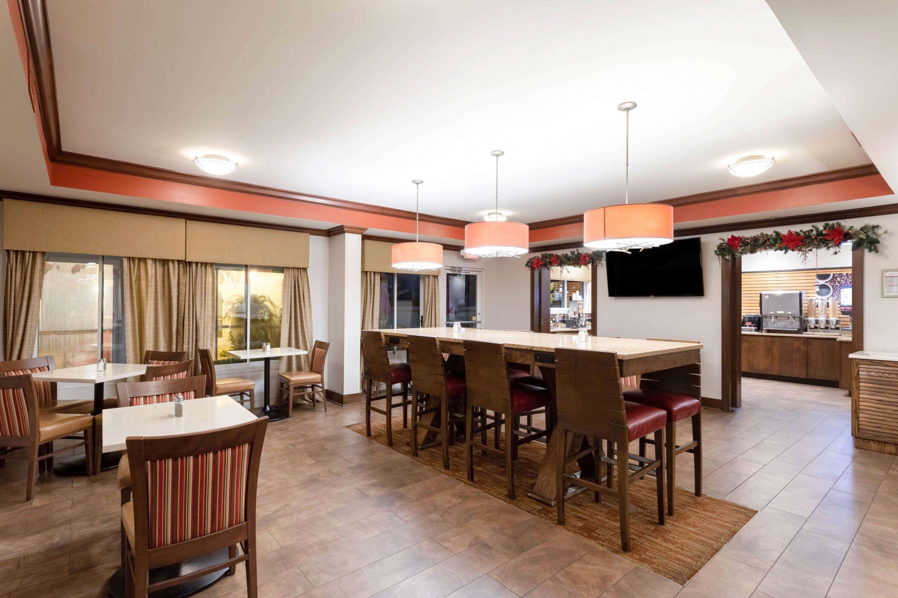 Un comedor de hotel con una larga mesa común, varios reservados y una barra.