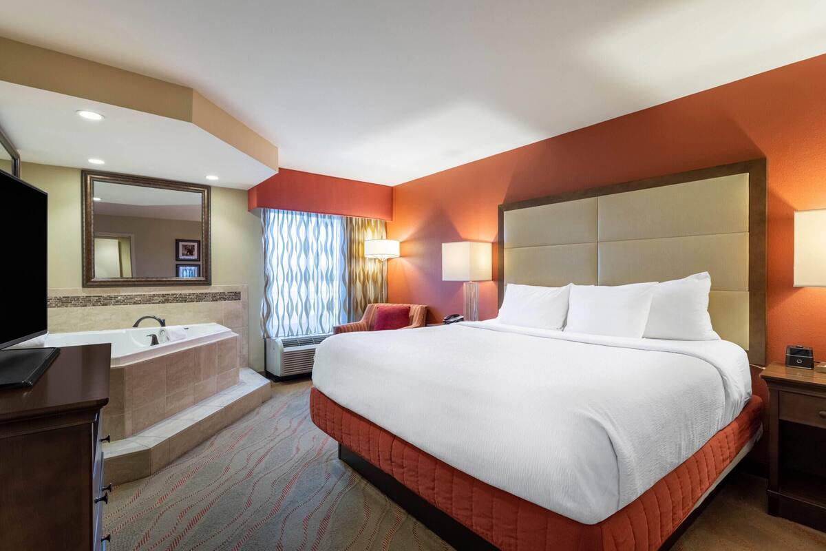 A hotel room with a large bed, a separate bathroom with a bathtub, a desk, and a television.