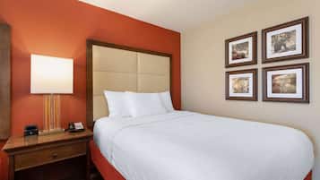 A hotel room with a large bed, a bedside table with a lamp, a phone, and a small drawer. There are four framed pictures on the wall.
