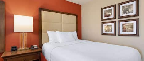 A hotel room with a large bed, a bedside table with a lamp, a phone, and a small drawer. There are four framed pictures on the wall.