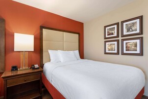 A hotel room with a large bed, a bedside table with a lamp, a phone, and a small drawer. There are four framed pictures on the wall.