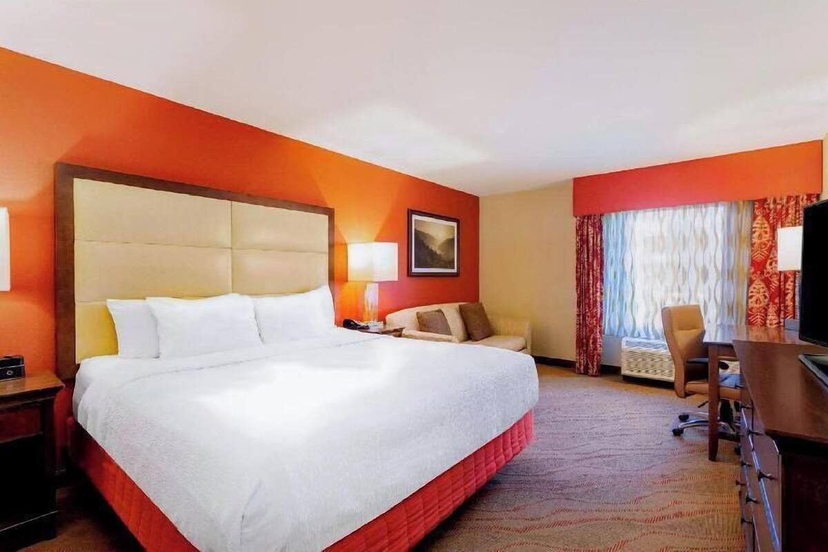 A hotel room with a large bed, a desk, a chair, a TV, and a window with curtains.