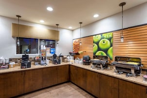 A self-service breakfast area with multiple food dispensers, a coffee machine, and a large poster advertising 'QUINTA'.