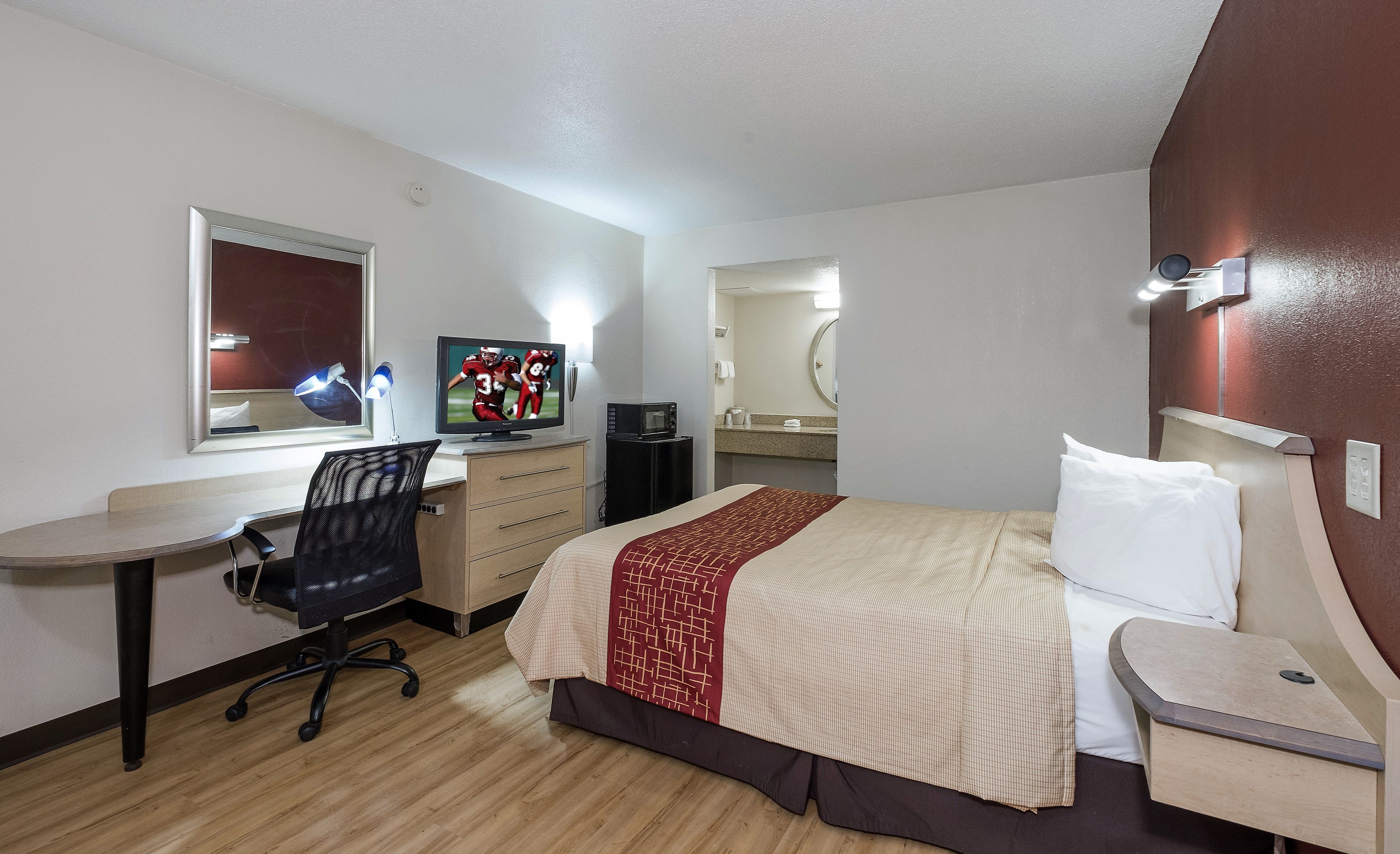 A hotel room with a bed, desk, chair, television, and a mirror.