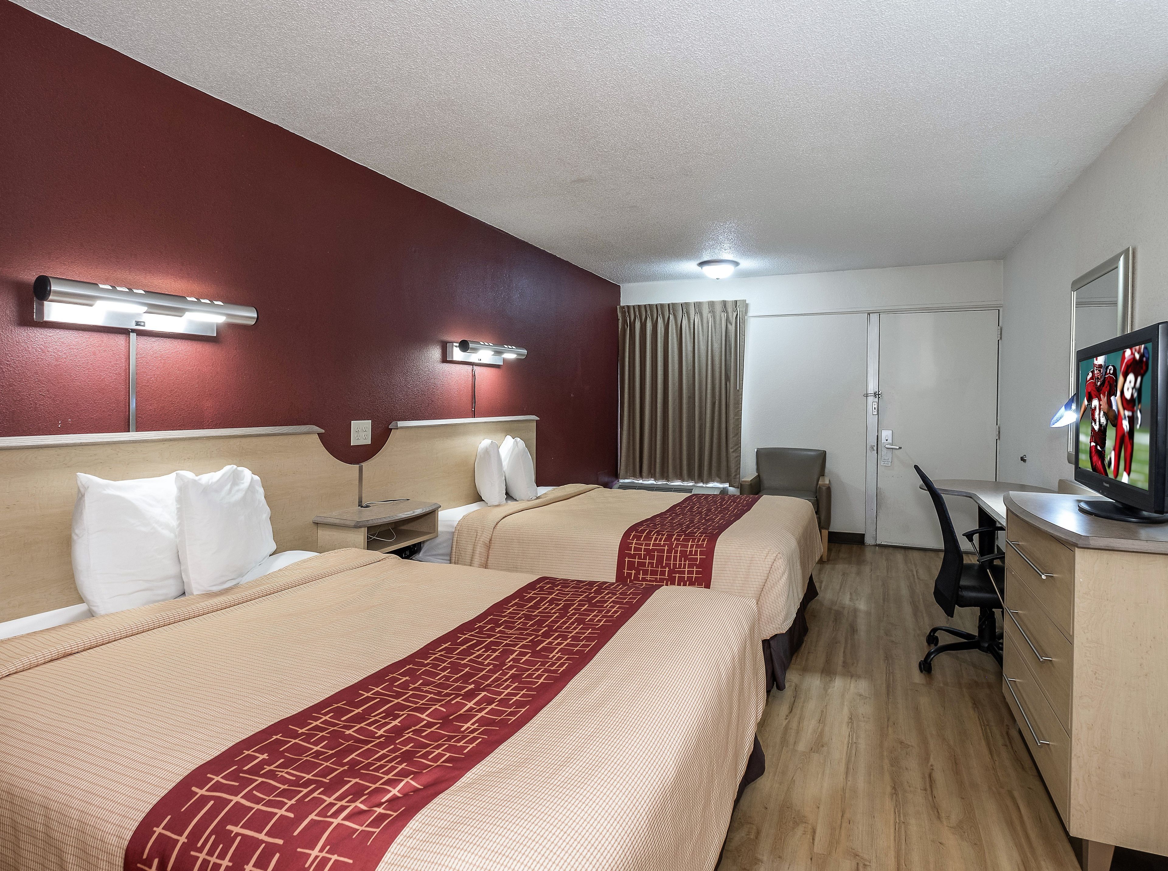 A hotel room with two beds, a desk, a chair, a television, and a window with curtains.