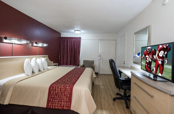 Una habitación de hotel con una cama, un escritorio, una silla, un televisor y una puerta.