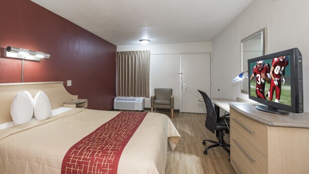 Habitación de hotel con cama, escritorio, silla, televisión y ventana con cortinas.