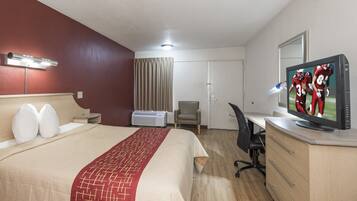 Habitación de hotel con cama, escritorio, silla, televisión y ventana con cortinas.