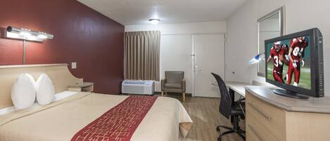 Habitación de hotel con cama, escritorio, silla, televisión y ventana con cortinas.