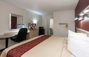 Une chambre d’hôtel avec un lit, un bureau avec un ordinateur, une télévision et un miroir.