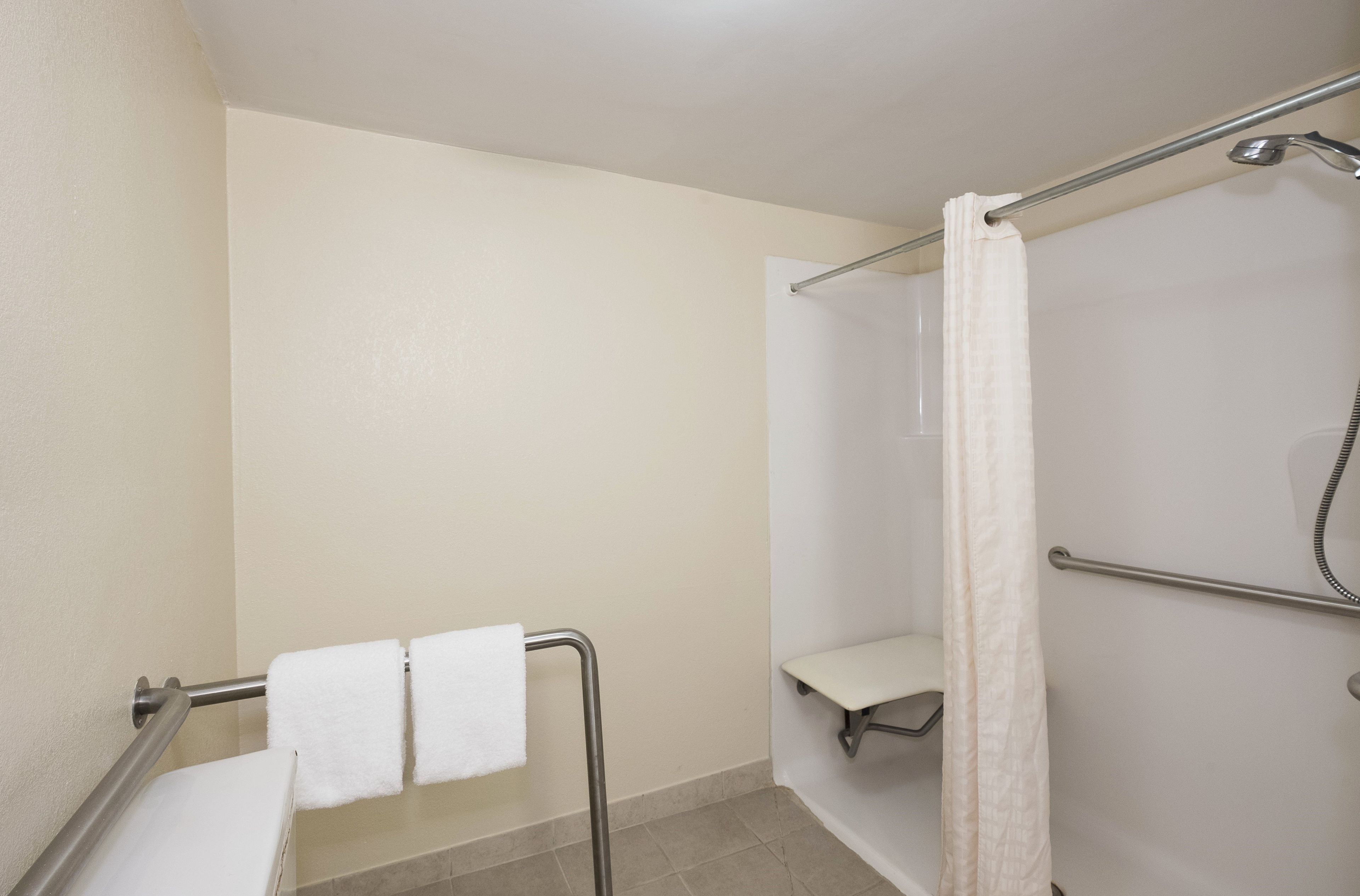 A bathroom with a shower, a grab bar, and a bench.