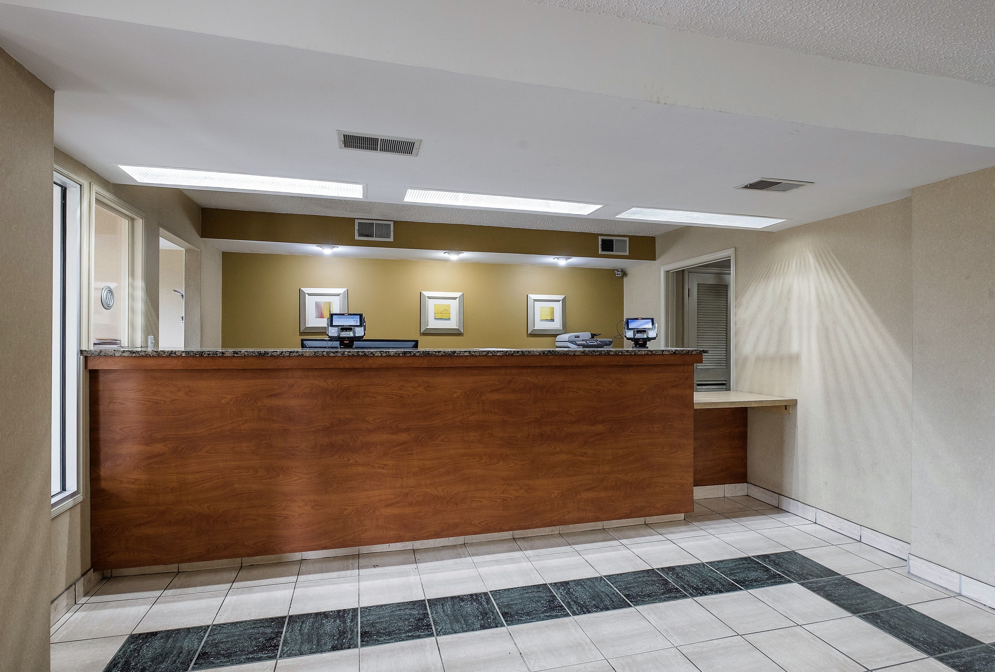 A reception desk with a wooden counter, a tiled floor, and a plain wall with three framed pictures.