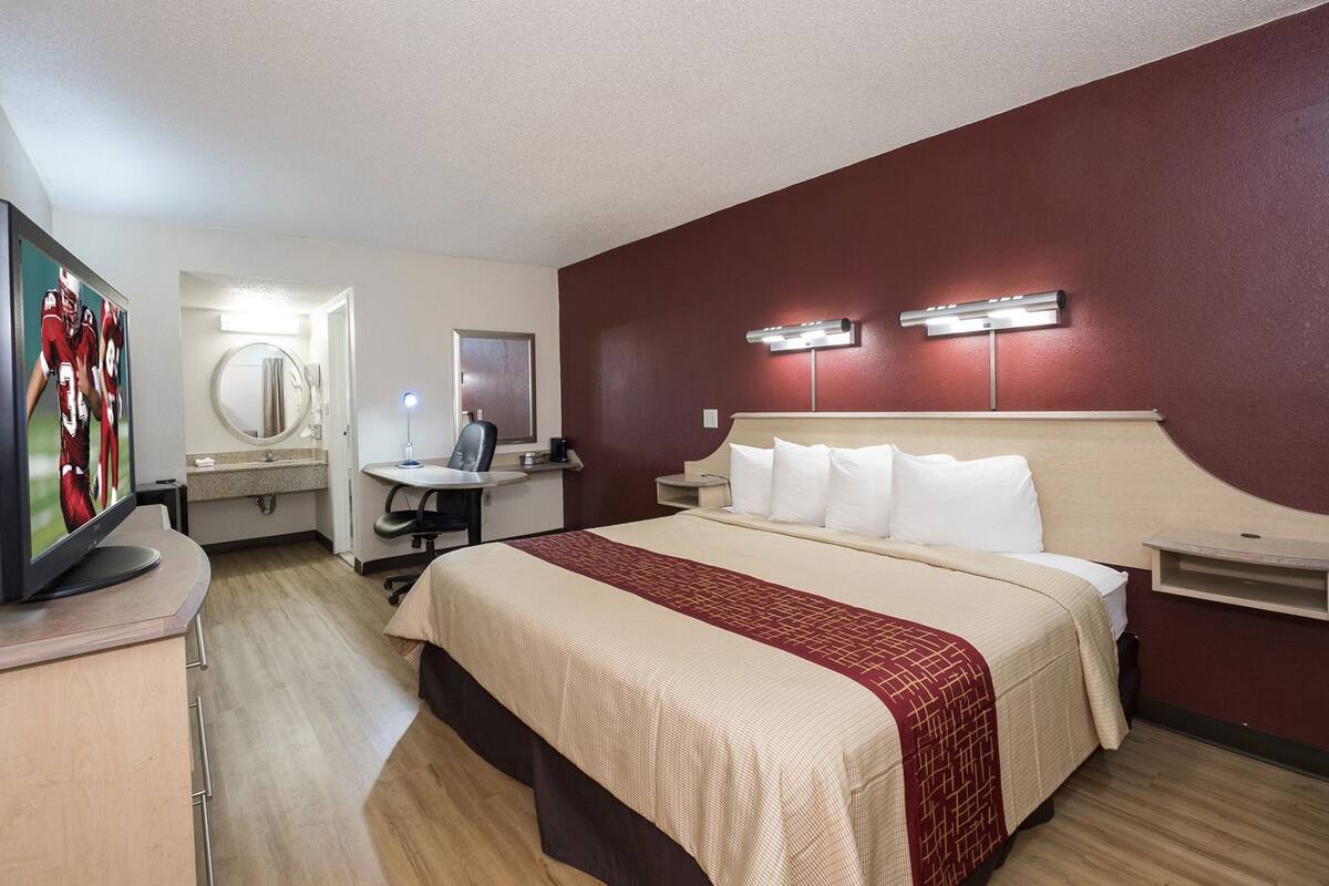 Ein Hotelzimmer mit einem Bett, einem Schreibtisch mit Stuhl, einem Fernseher und einem Spiegel.