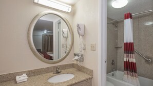 A bathroom with a round mirror, a sink, a hairdryer, and a shower with a curtain. - Red Roof Inn Hagerstown - Williamsport, MD (Williamsport)
