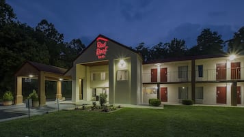 Een motel met een neonbord, een overdekte parkeerplaats en een verzorgd gazon.