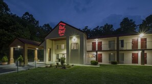 Un motel con un letrero de neón, una zona de estacionamiento techada y un césped cuidado.