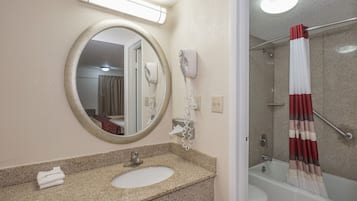 A bathroom with a round mirror, a sink, a hairdryer, and a shower with a curtain.