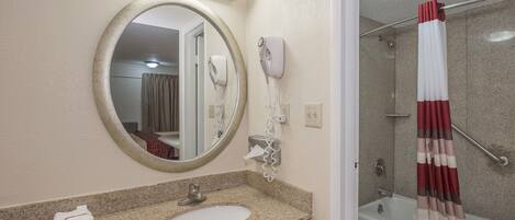 A bathroom with a round mirror, a sink, a hairdryer, and a shower with a curtain.