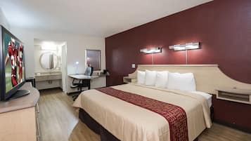 A hotel room with a bed, a desk with a computer, a mirror, and a television.