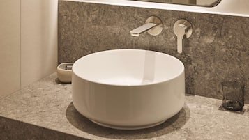 A bathroom with a large white basin, a towel dispenser, and a glass of water on the countertop.