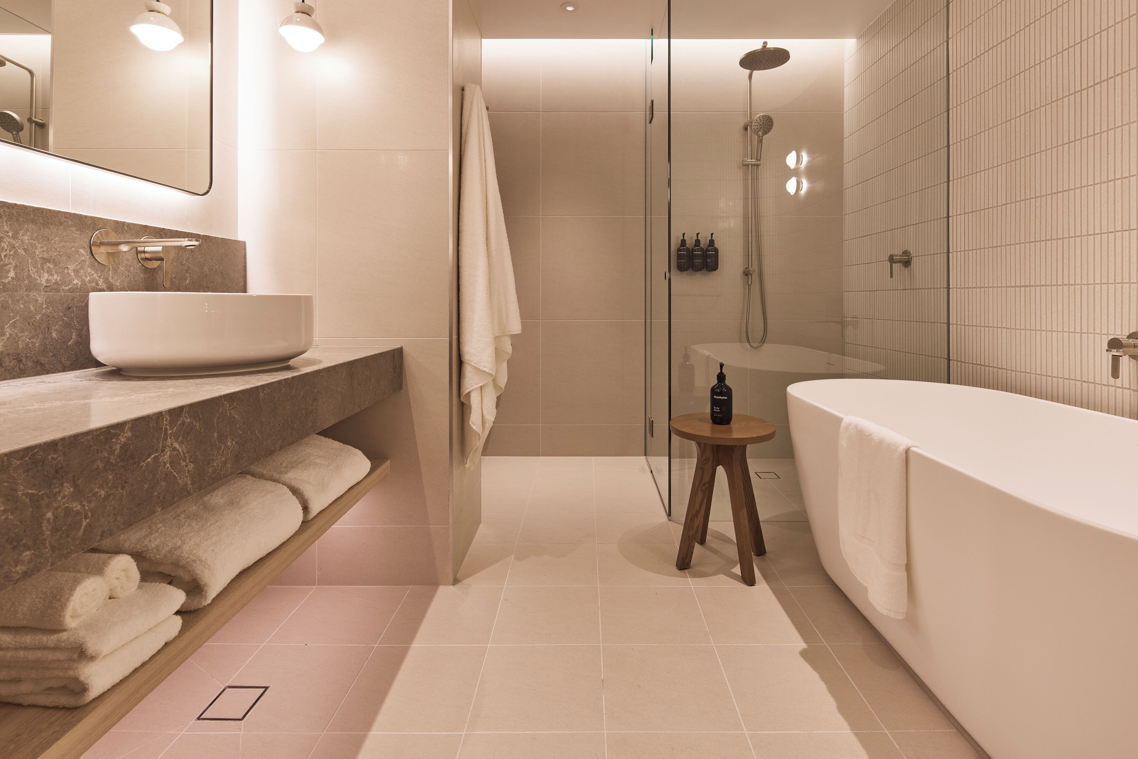 Un baño moderno con una bañera grande, cabina de ducha con paredes de vidrio, tocador de mármol con lavabo integrado y toallas ordenadas en un estante.
