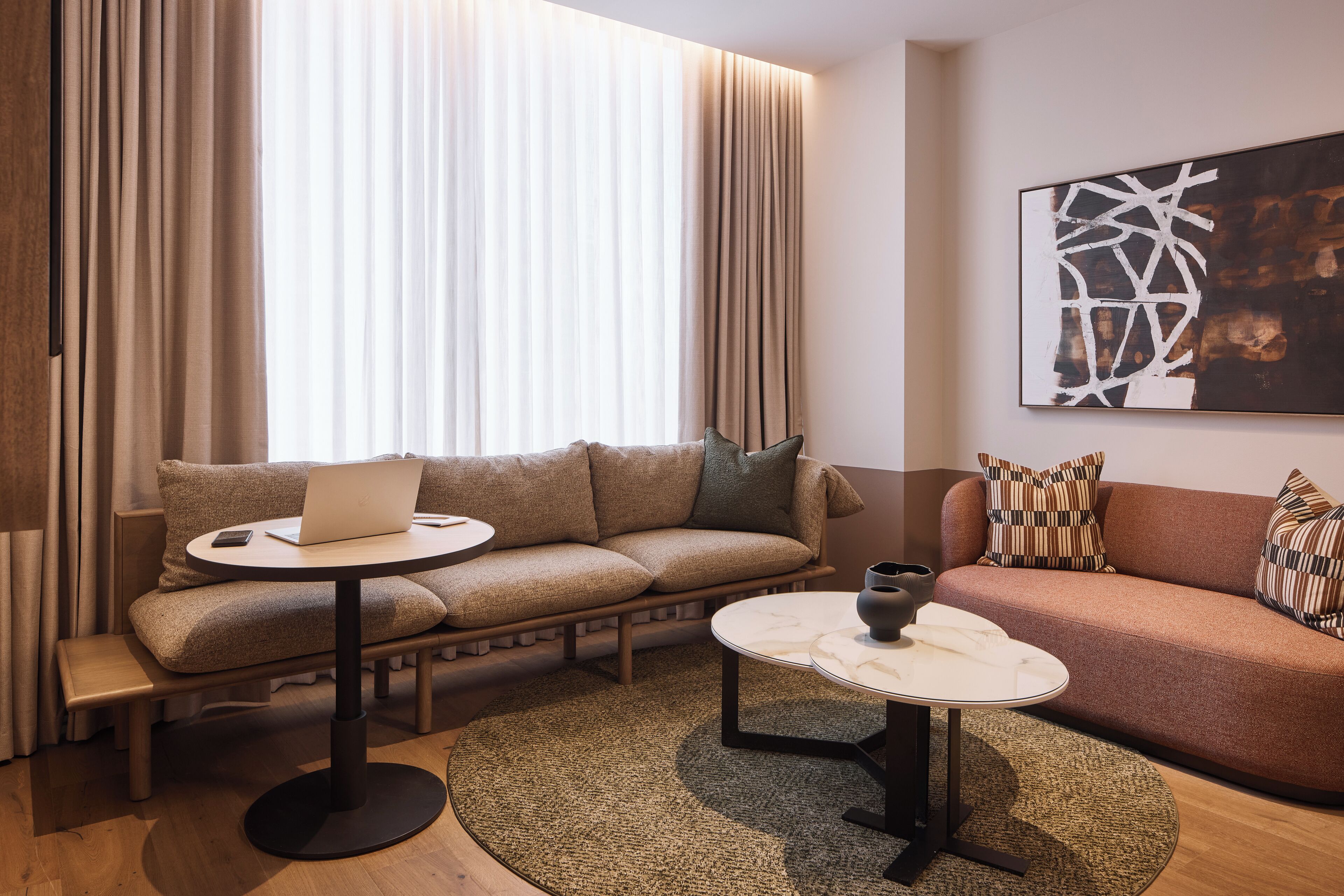 A modern living room with a sofa, a coffee table, and a laptop on a small round table.
