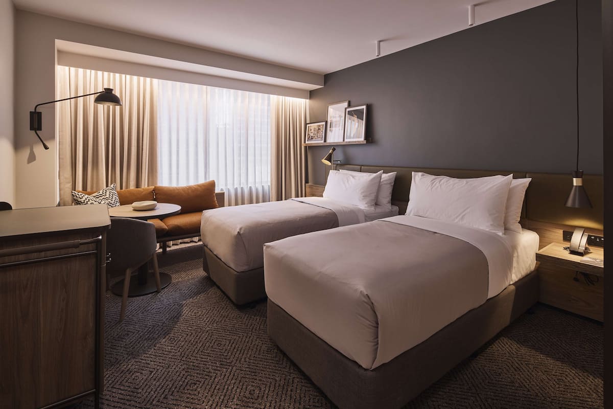 Ein Hotelzimmer mit zwei Betten, einem Schreibtisch, einem Stuhl und einem Fenster mit Vorhängen.