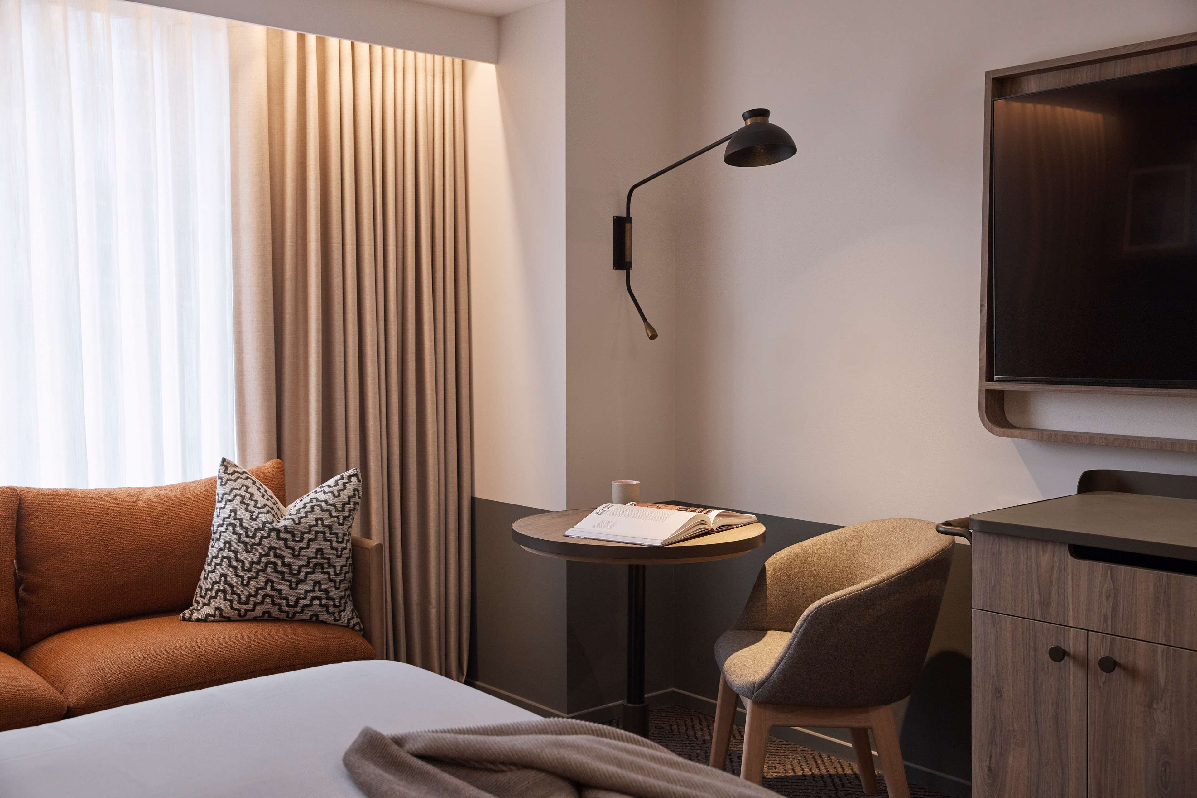 Une chambre d’hôtel comprenant un lit, un canapé, une chaise, une petite table, une lampe et un téléviseur.