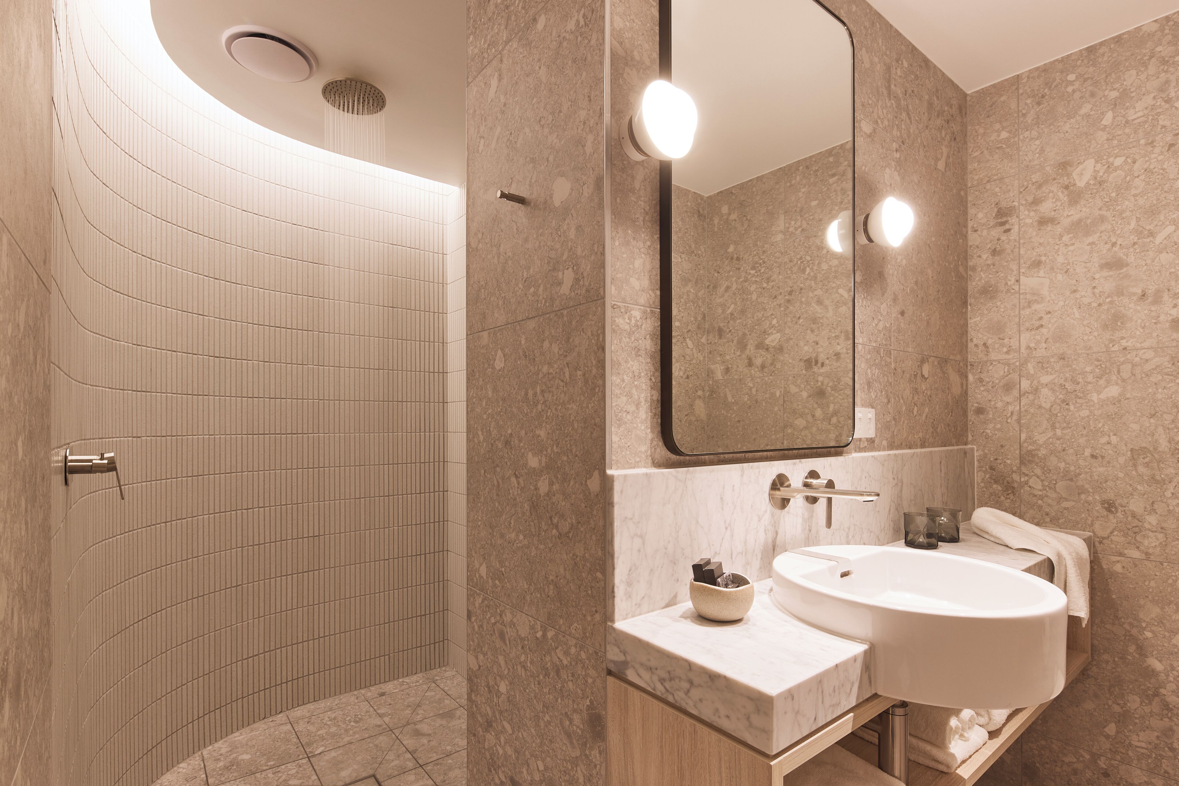 Een moderne badkamer met een douche in boogvorm, een grote spiegel en een wastafel met een marmeren aanrecht.