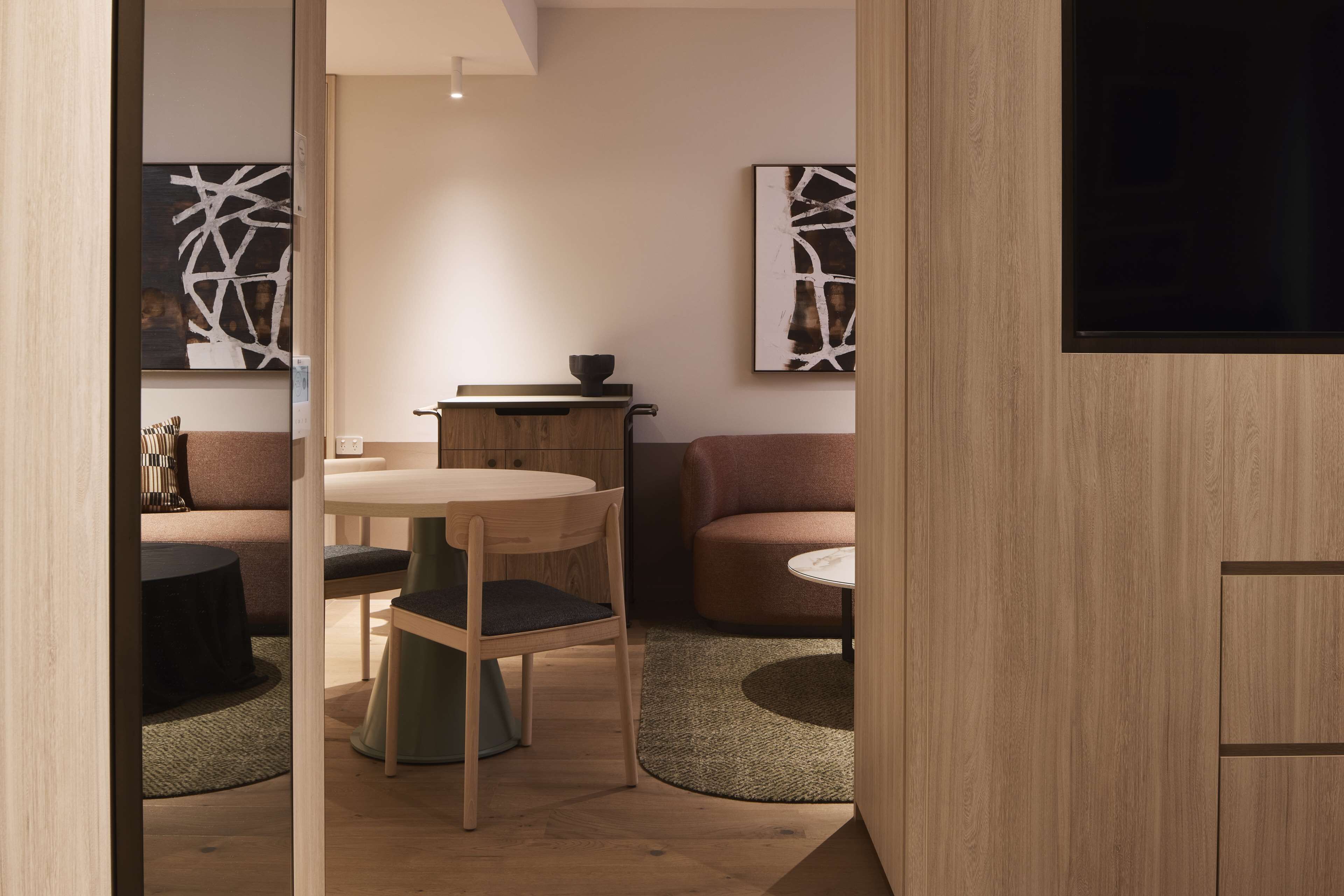 Een moderne woonkamer met een houten vloer, een ronde eettafel, twee banken en abstracte wanddecoratie.