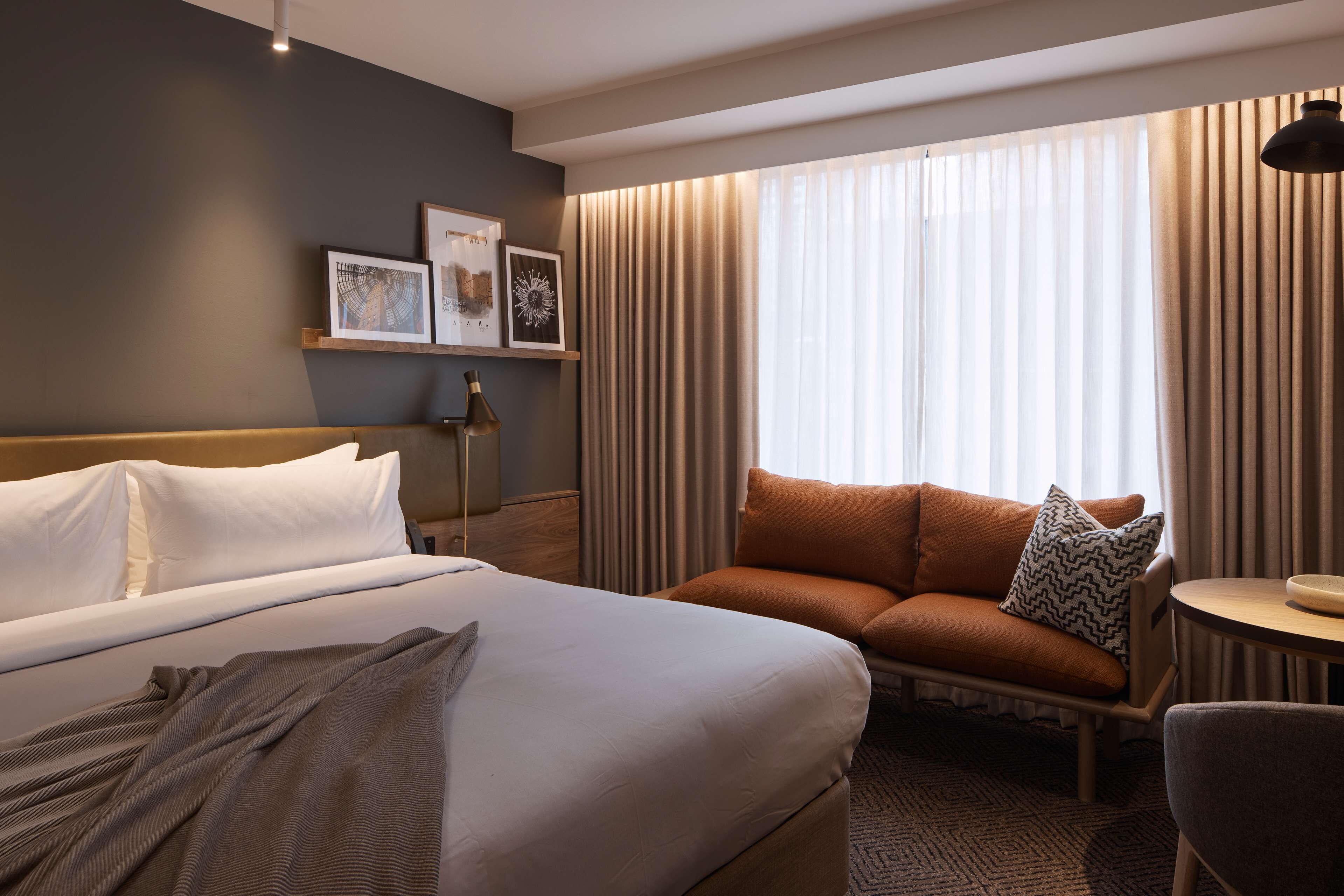 A hotel room with a large bed, a sofa, a small table, and a window with curtains.