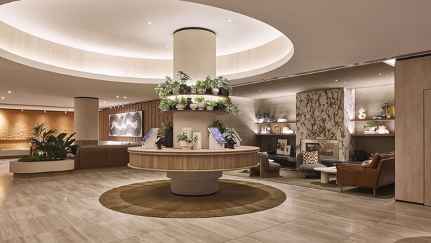 A modern lobby with a central circular reception desk, a large wall-mounted artwork, and a seating area with sofas and a coffee table.