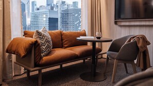 A modern hotel room with a sofa, a chair, a small table, and a TV.