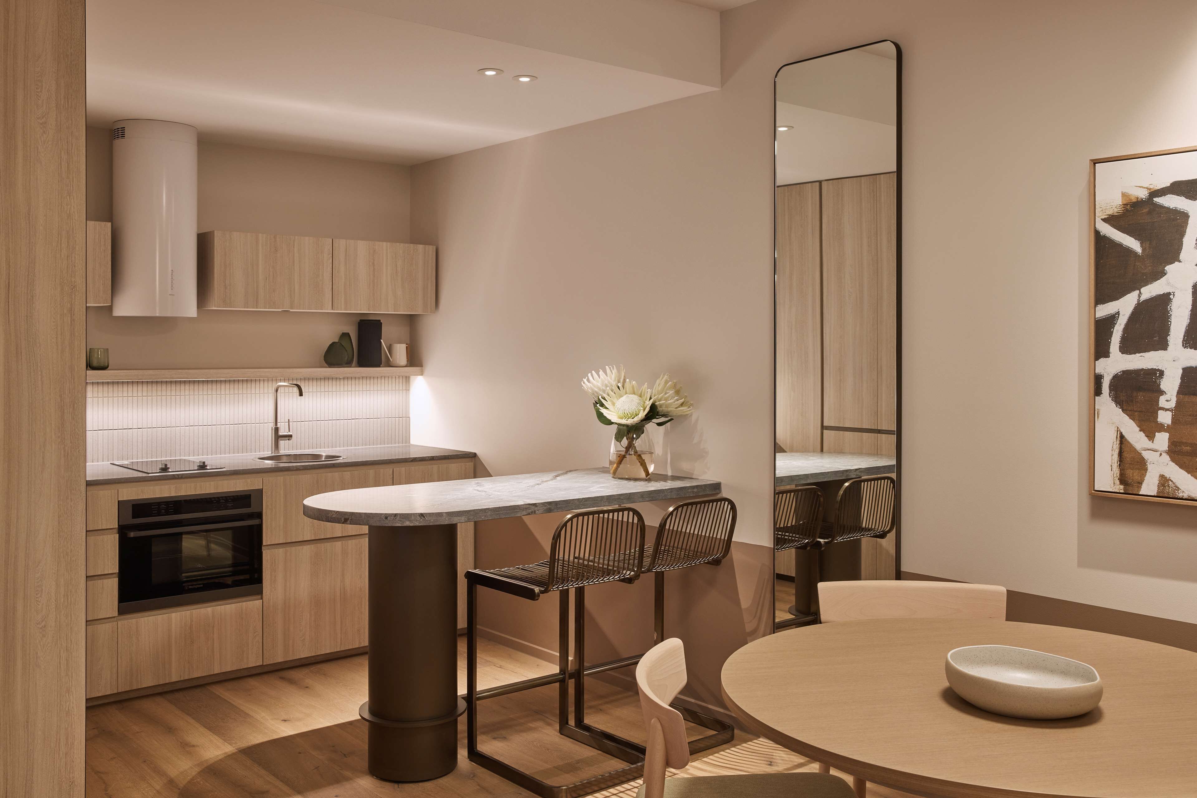 A modern kitchen with a central island, built-in oven, and a dining area with a round table and chairs.