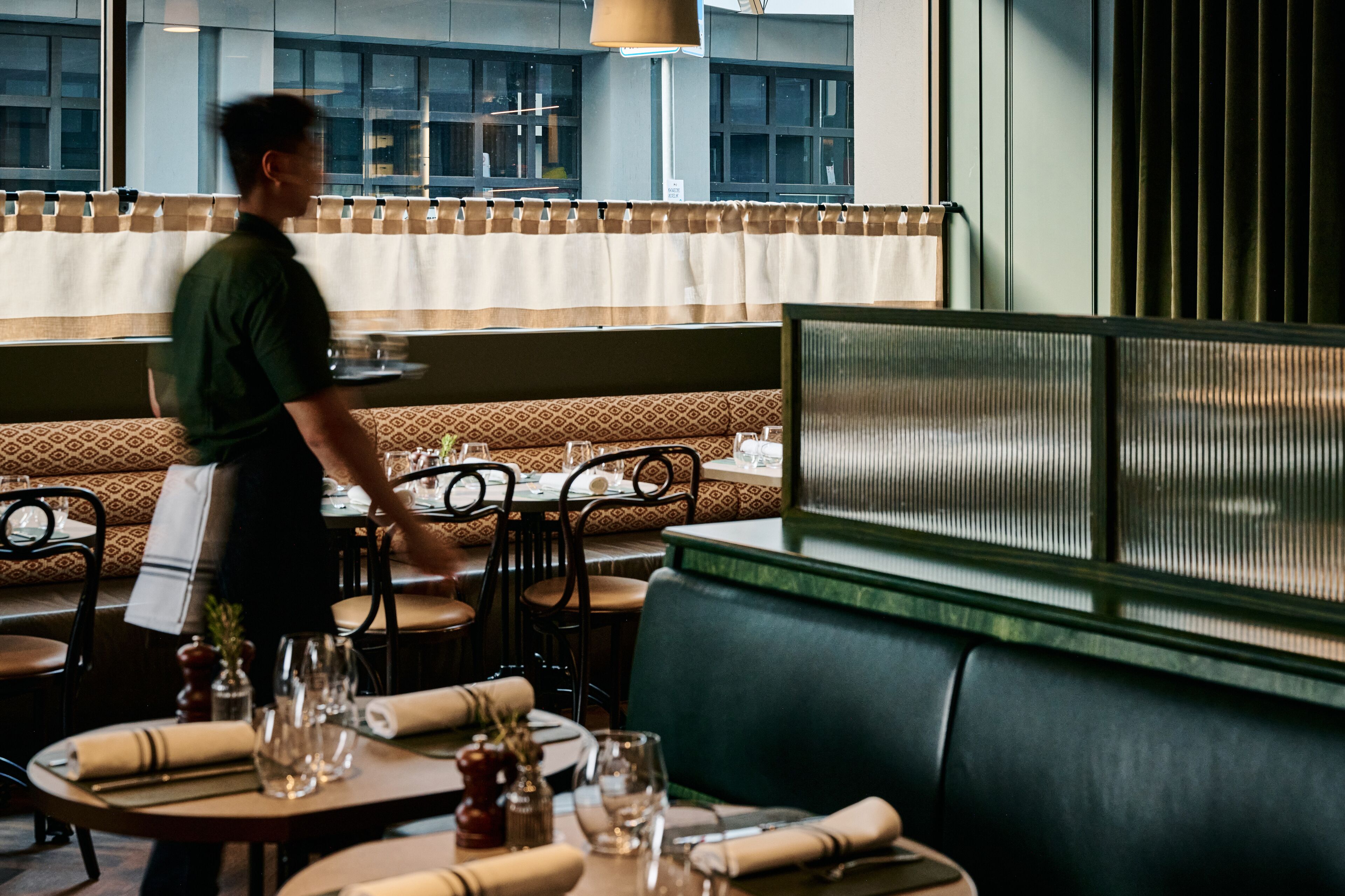A restaurant with booths, tables, and a waiter.