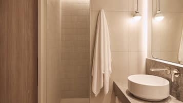 A modern bathroom with a wooden wall, a tiled shower area, a white sink, and a towel hanging on the wall.