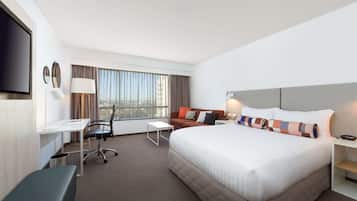 Ein Hotelzimmer mit einem großen Bett, einem Schreibtisch, einem Sessel, einer Couch und einem Fernseher.