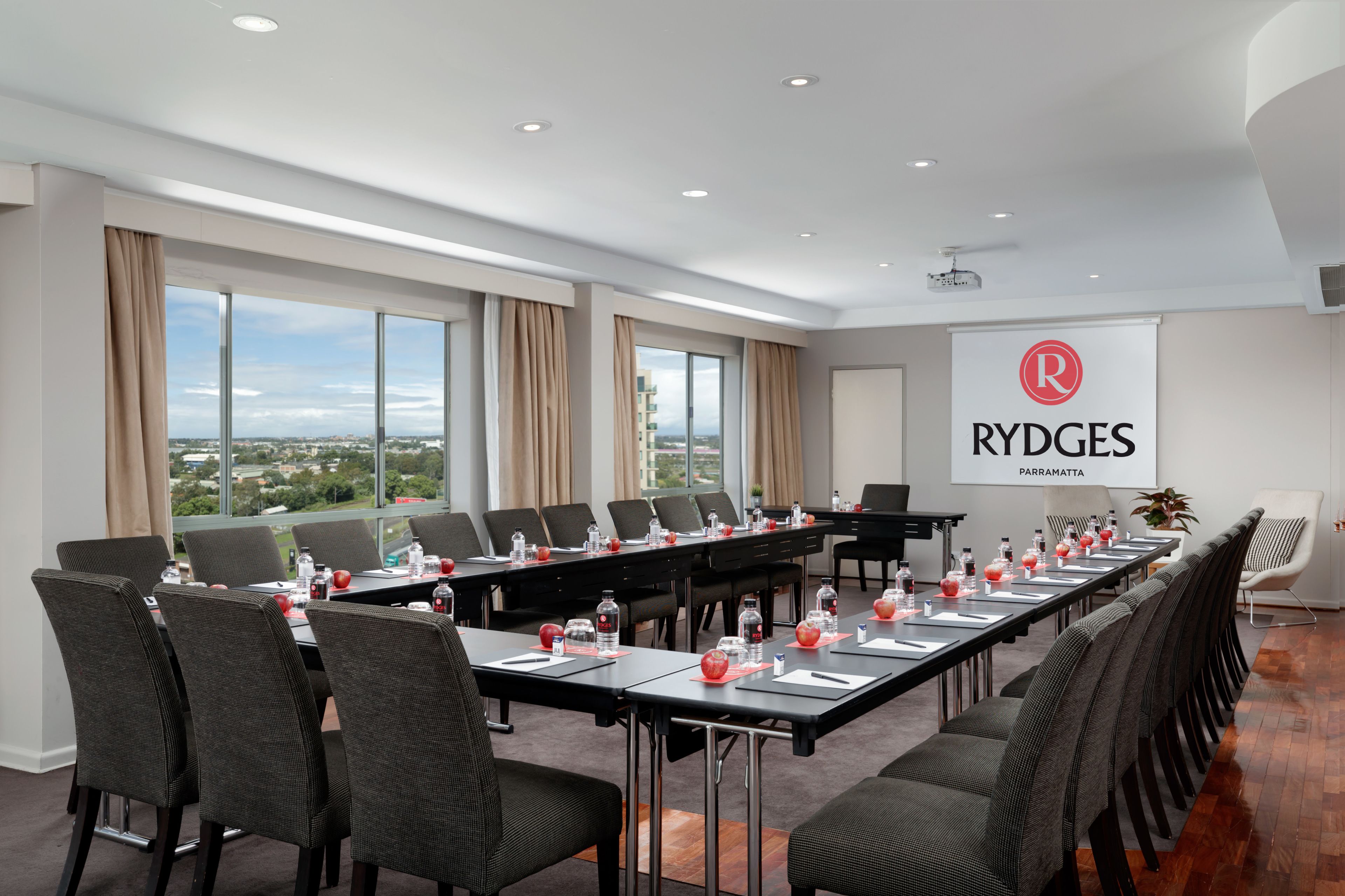 A conference room with a long table, chairs, and a projector screen displaying the Rydges logo.