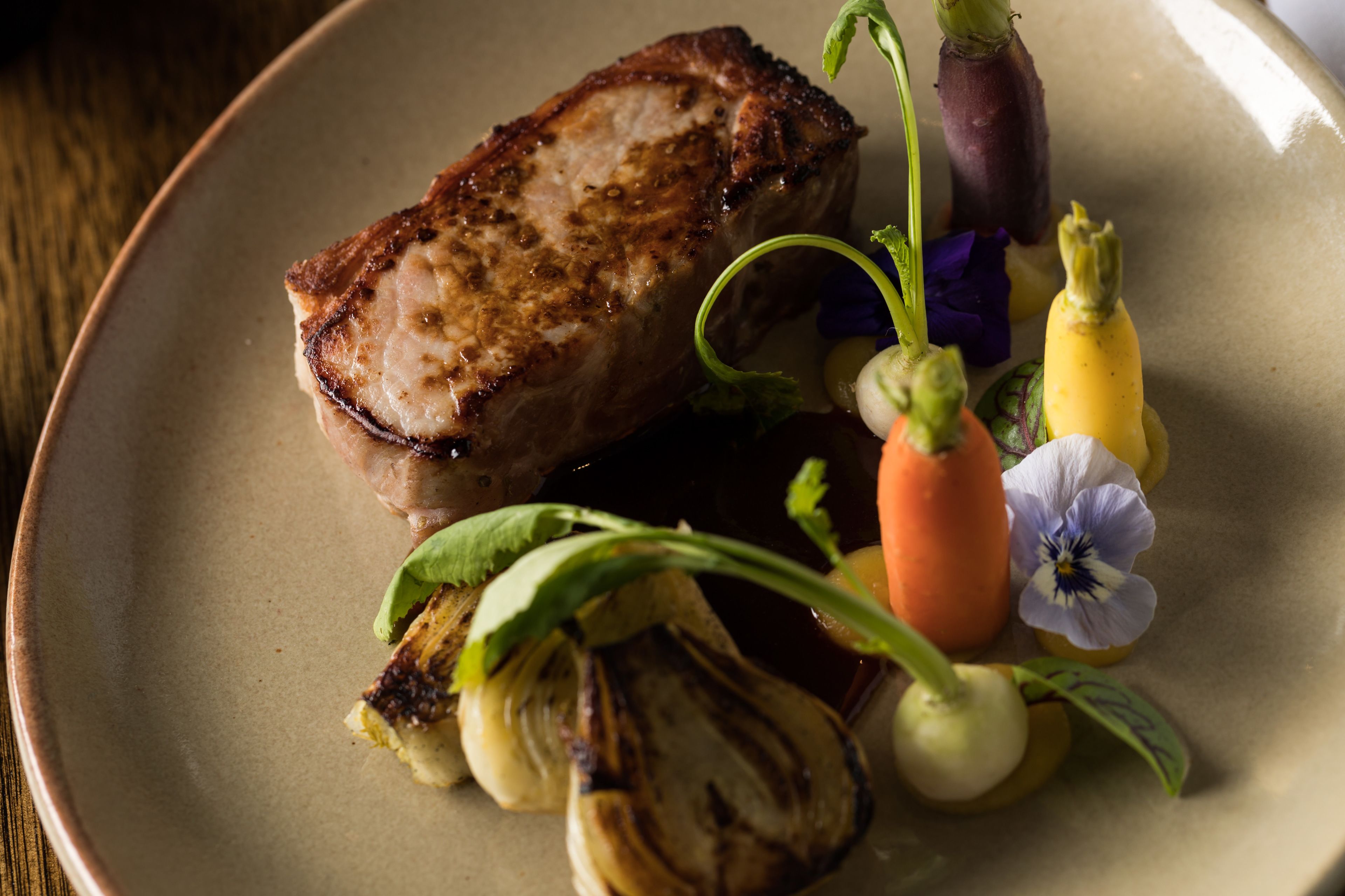A plate with grilled meat, vegetables, and a flower.