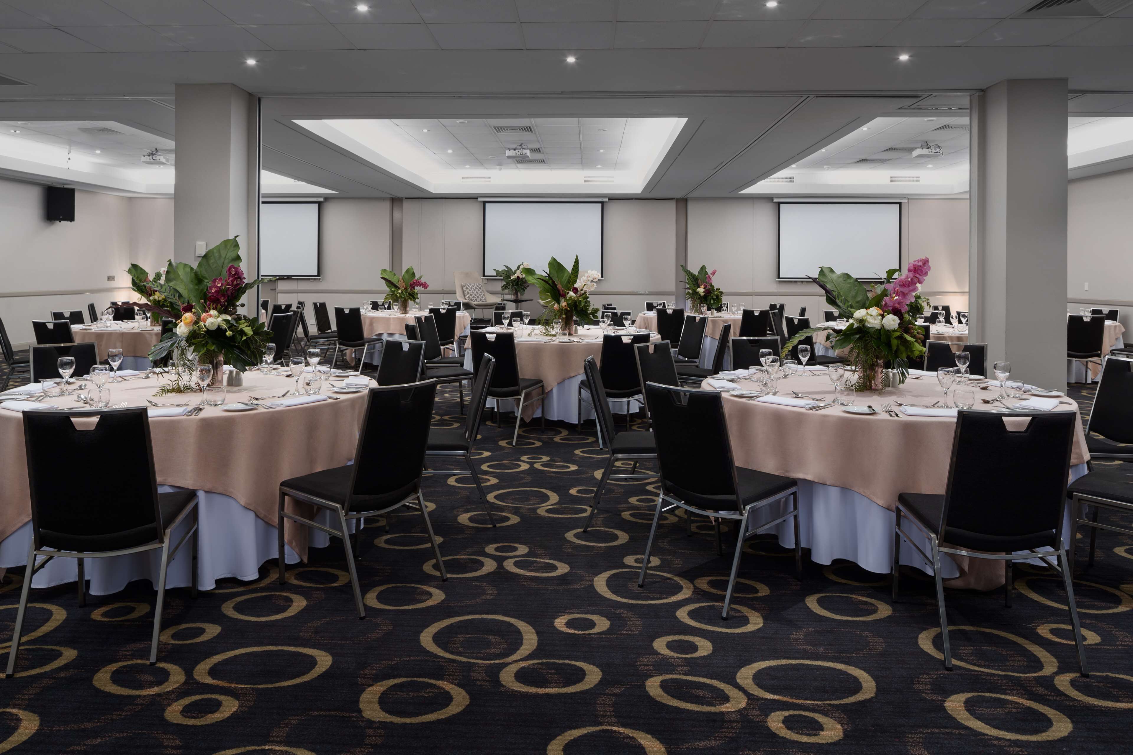 Une salle de conférence dotée de plusieurs tables rondes, chacune étant agrémentée de chaises, de nappes blanches et de compositions florales.