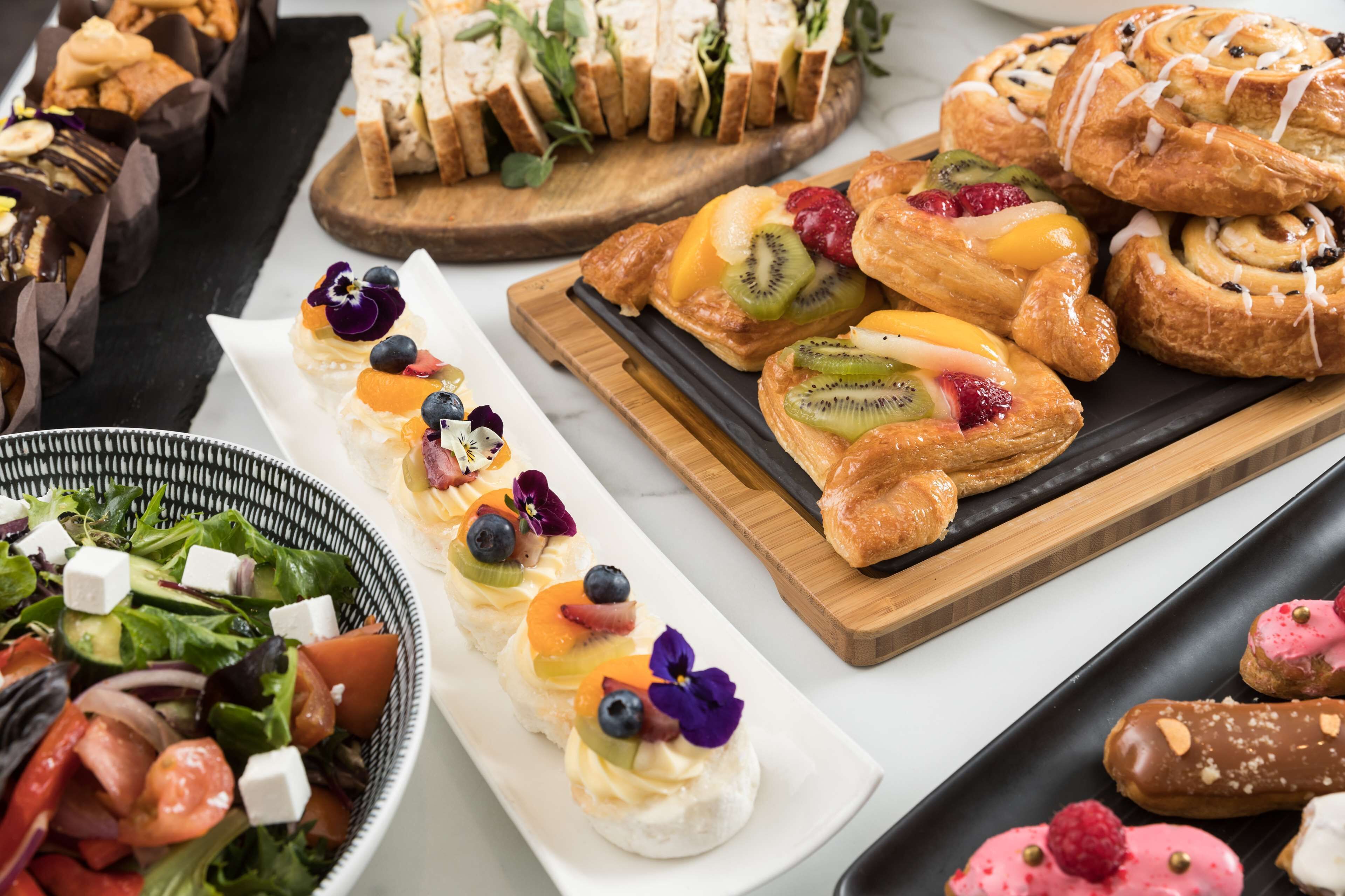 A variety of pastries and desserts on display, including fruit-topped pastries and a selection of sandwiches.