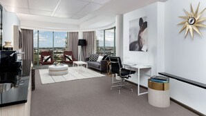 Una habitación de hotel moderna con techo curvo, un ventanal grande con vistas a la ciudad, un escritorio con silla, un sofá con cojines decorativos y una decoración de pared con forma de estrella.
