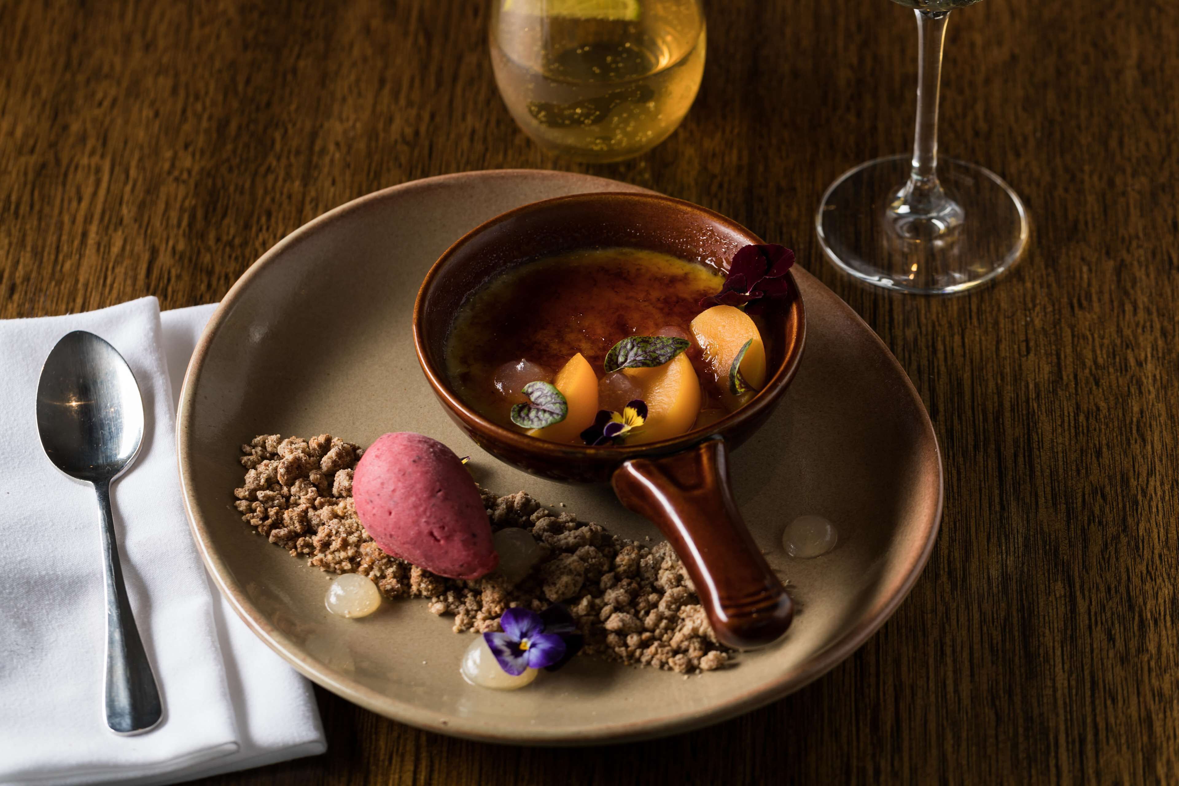 A dessert plate with a bowl of soup, a scoop of ice cream, and garnishes on a wooden table.