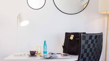 A room with a white table, a black checkered chair, a black handbag, a blue bottle, a purple cup, a pair of glasses, and two round mirrors on the wall.