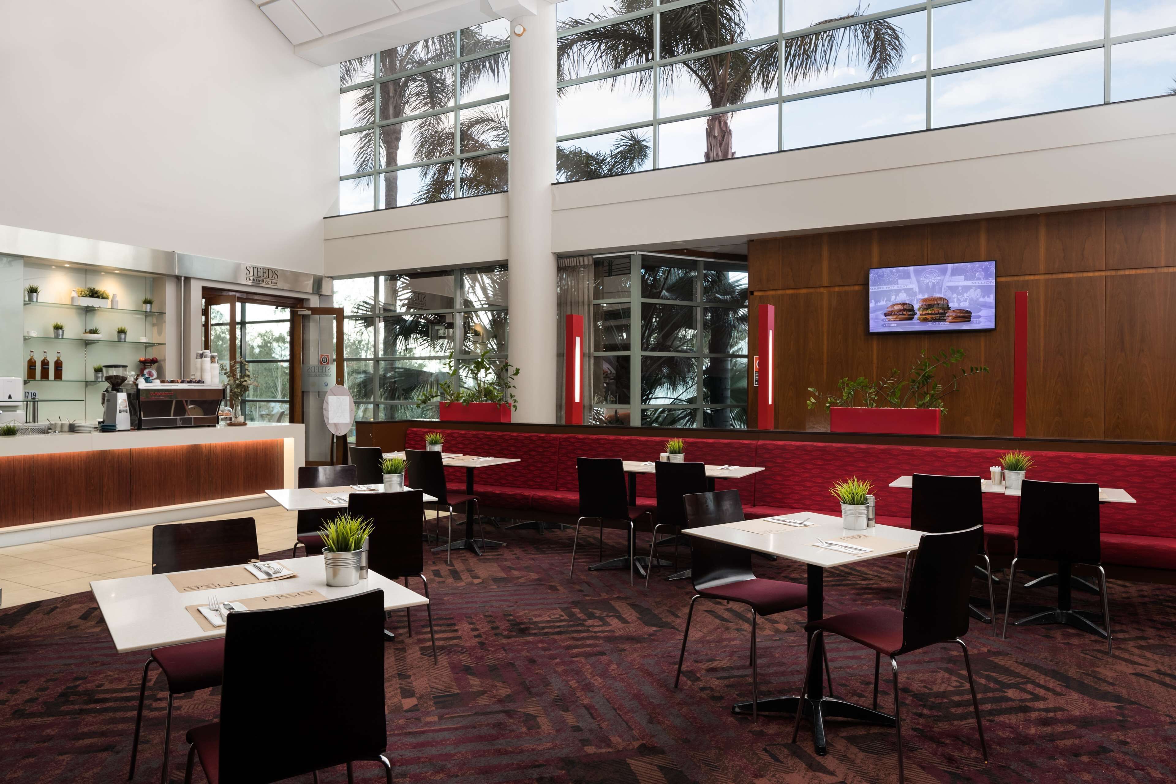 A spacious indoor area with a reception desk, multiple tables and chairs, and large windows offering views of palm trees.