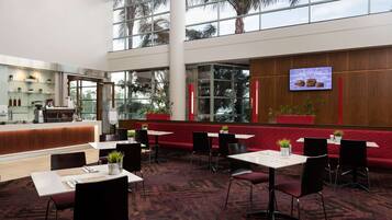 A spacious indoor area with a reception desk, multiple tables and chairs, and large windows offering views of palm trees.