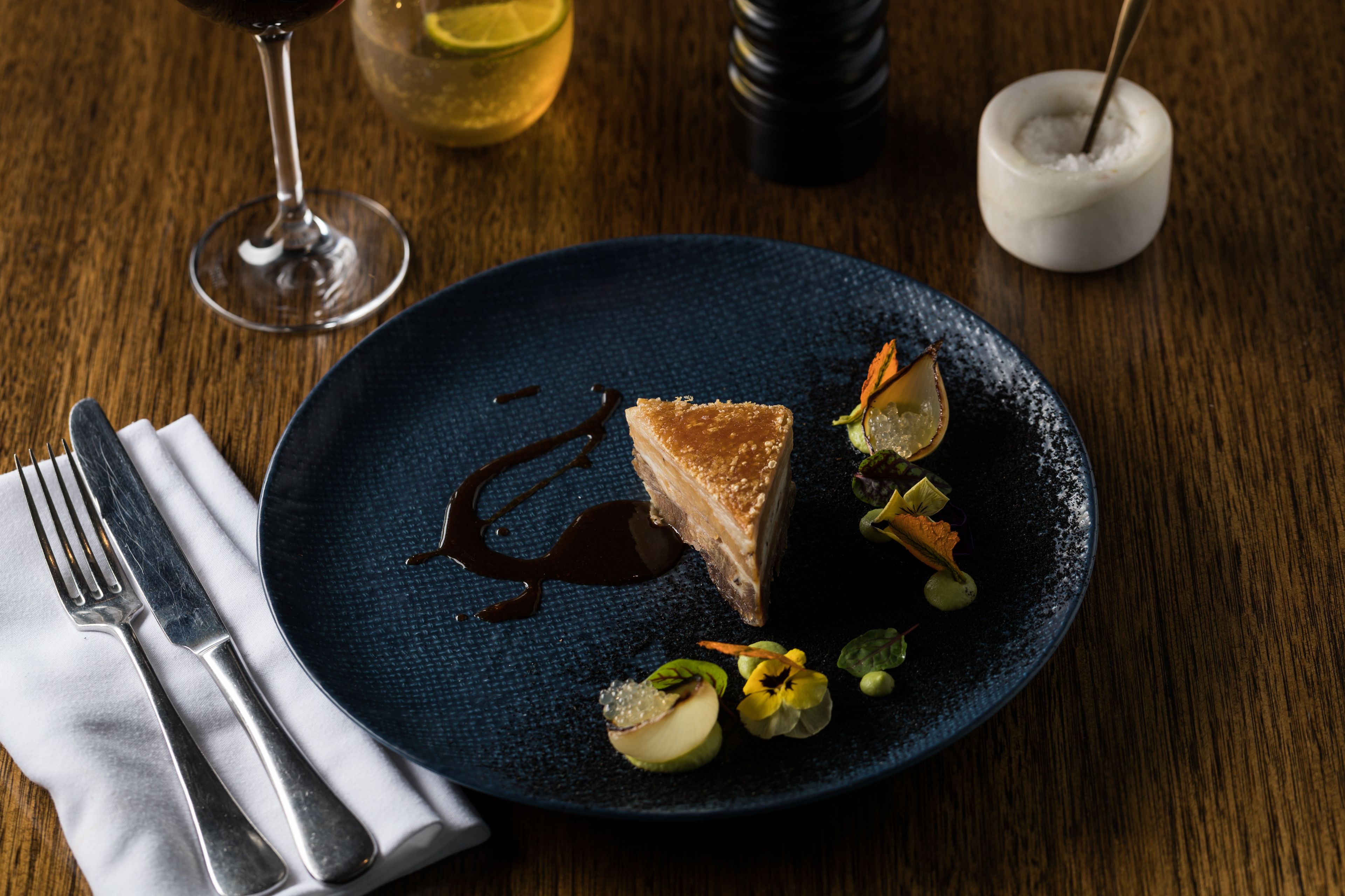 A dessert plate with a slice of cake, chocolate sauce, and garnishes on a dark plate.