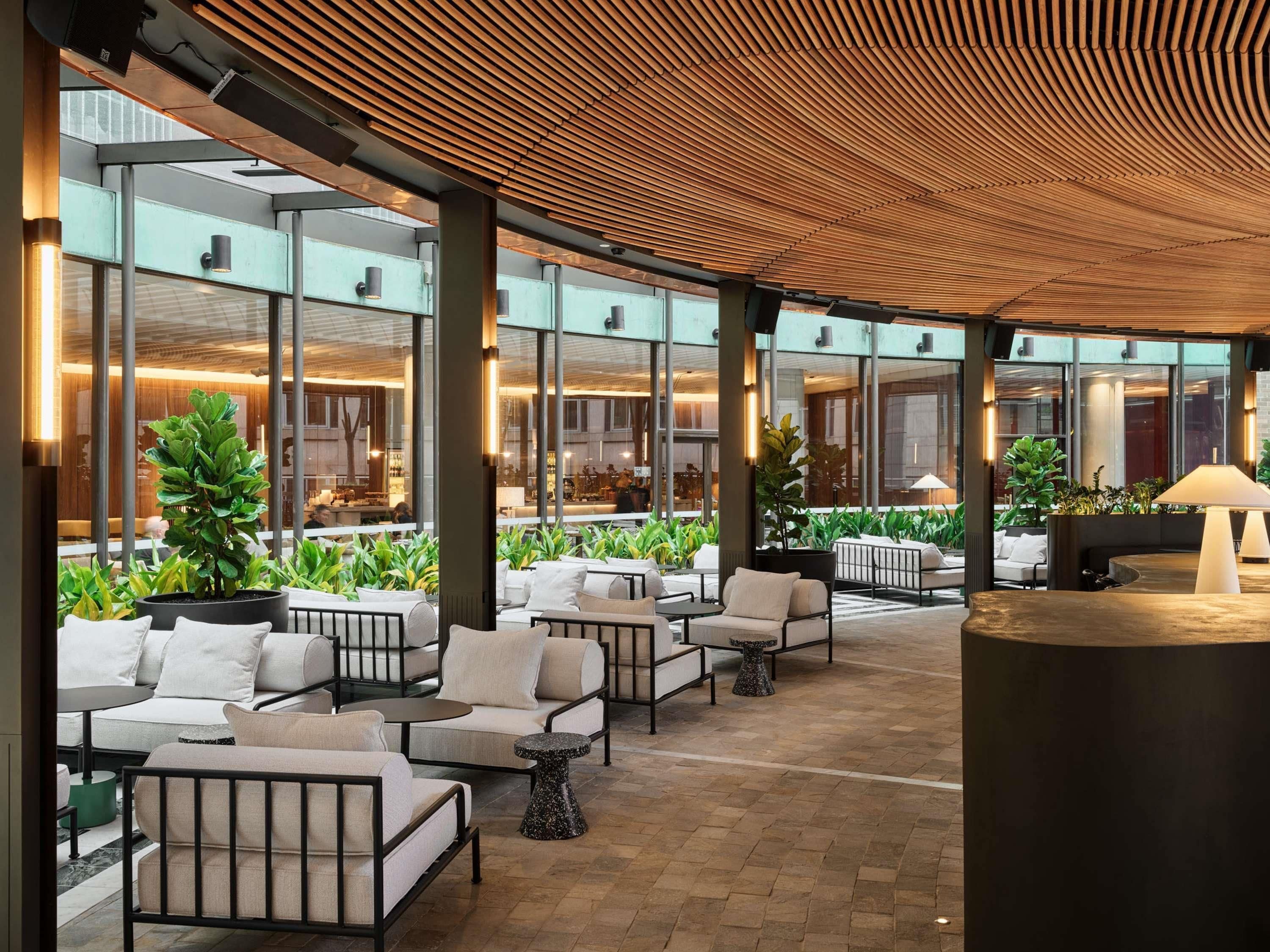 An outdoor seating area with modern furniture, large windows, and indoor lighting.