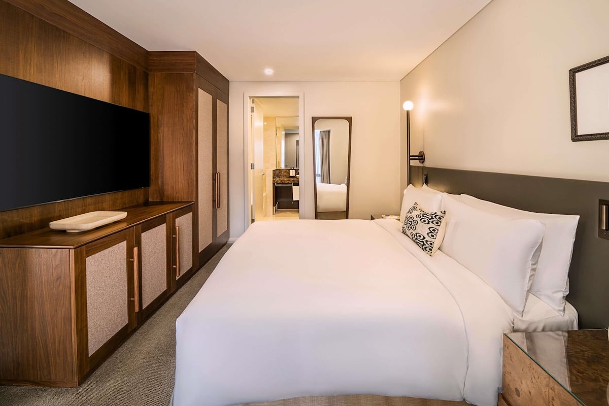 A hotel room with a large bed, a TV mounted on the wall, a wooden cabinet, and a mirror.