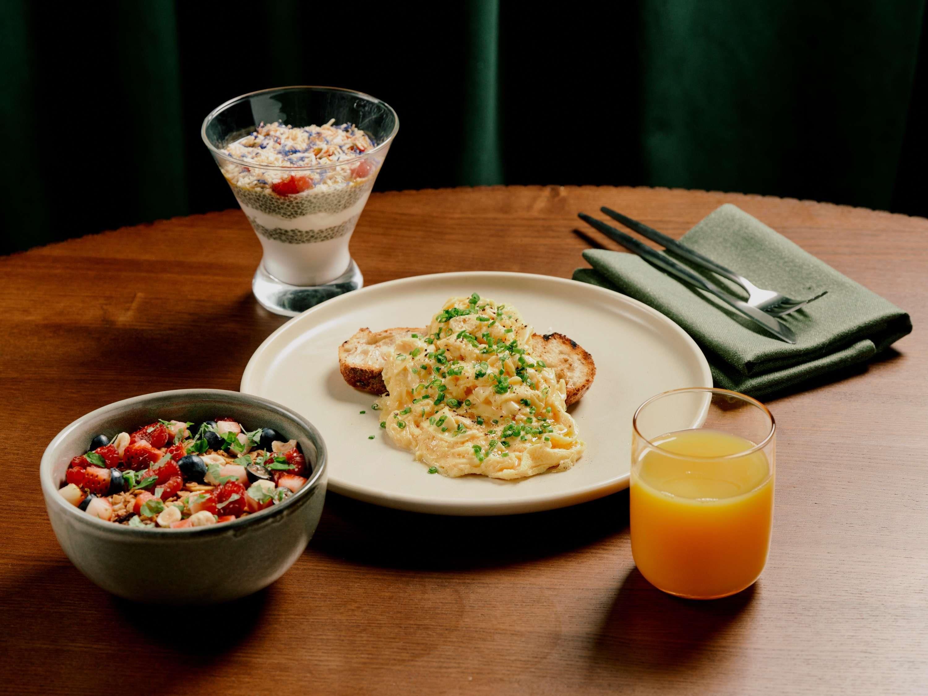 A dining table with a plate of food, a bowl of salad, a glass of orange juice, and a dessert in a glass.